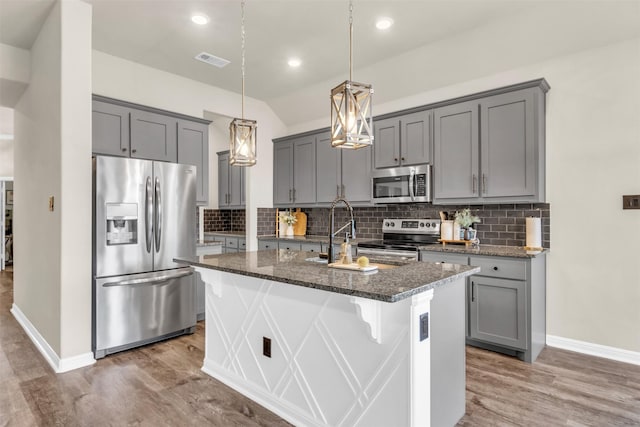 kitchen with visible vents, hanging light fixtures, appliances with stainless steel finishes, dark stone countertops, and a center island with sink