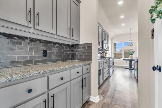 kitchen with appliances with stainless steel finishes, backsplash, gray cabinetry, and light stone countertops