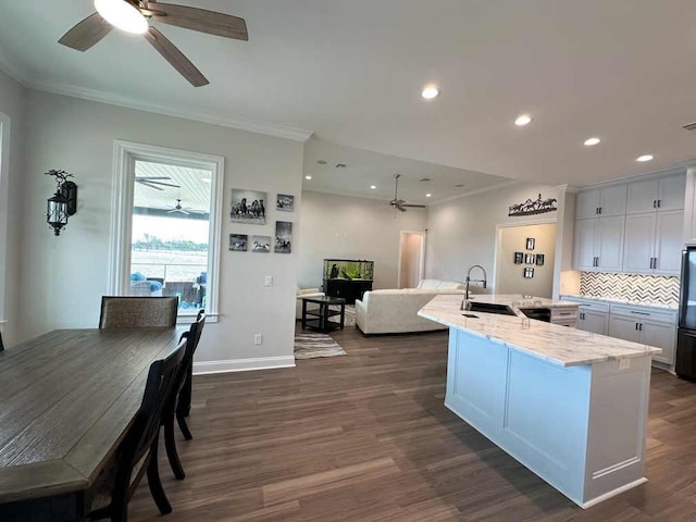 kitchen with crown molding, dark wood-style flooring, ceiling fan, a sink, and an island with sink