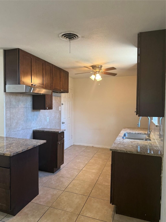 kitchen with light tile patterned flooring, a sink, visible vents, dark brown cabinets, and light stone countertops