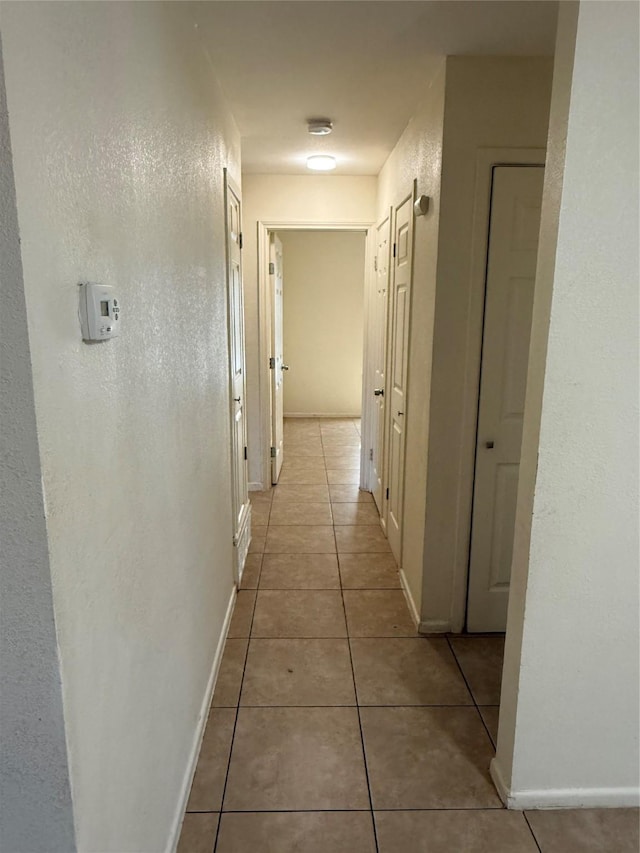 corridor with a textured wall, baseboards, and light tile patterned floors