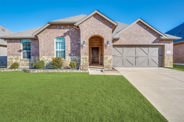 french country inspired facade with a garage, a front yard, concrete driveway, and brick siding