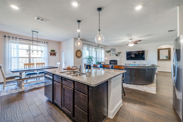 kitchen featuring visible vents, a kitchen island with sink, stainless steel appliances, dark brown cabinets, and a sink