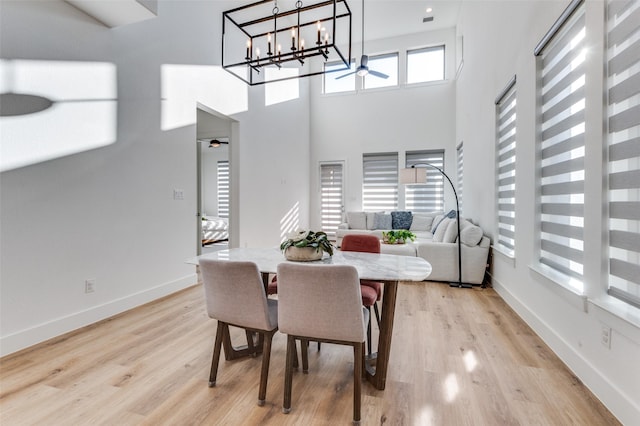 dining space featuring light wood-type flooring, ceiling fan, a towering ceiling, and baseboards