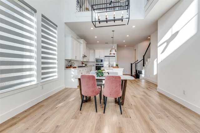 dining space with stairs, a high ceiling, light wood-style flooring, and baseboards