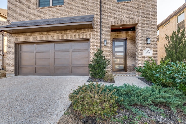 entrance to property with a garage, brick siding, and driveway