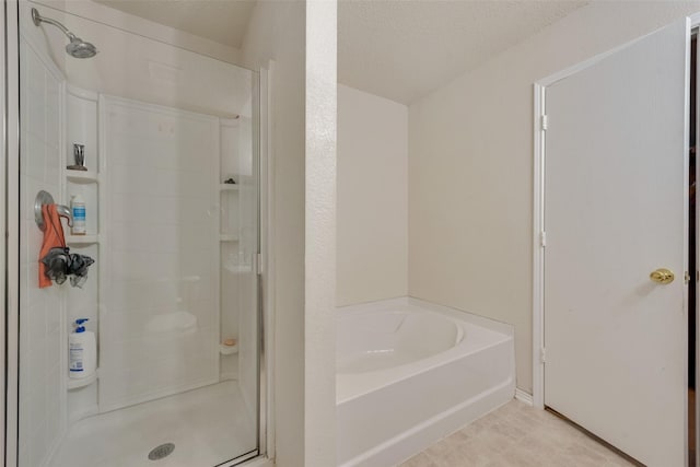 full bathroom featuring a textured ceiling, a shower stall, and a bath