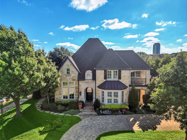 french country inspired facade featuring stone siding, a front yard, a standing seam roof, and metal roof