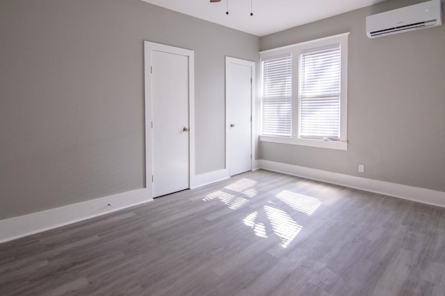 unfurnished bedroom featuring ceiling fan, a wall unit AC, wood finished floors, and baseboards