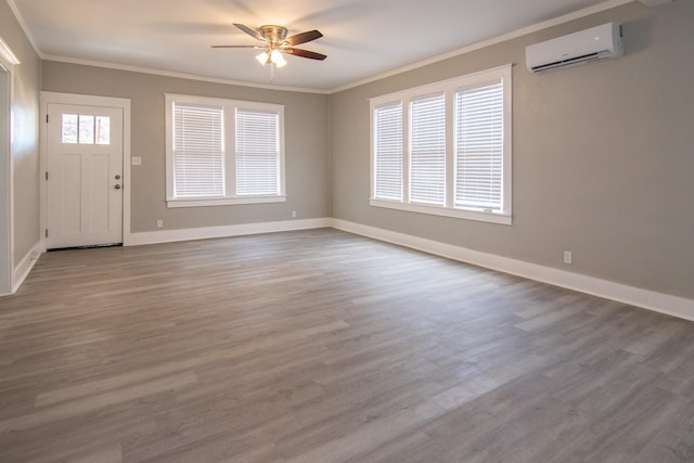 entrance foyer featuring a wall unit AC, wood finished floors, a ceiling fan, baseboards, and ornamental molding