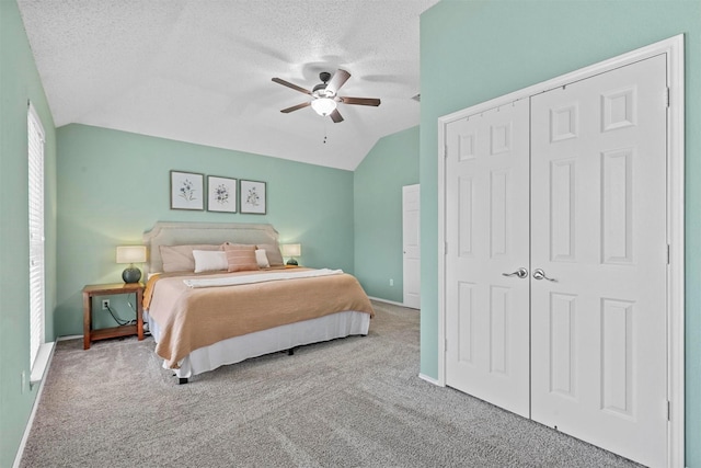 bedroom with a textured ceiling, a ceiling fan, vaulted ceiling, a closet, and carpet