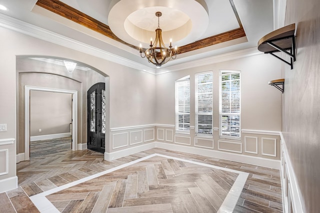 unfurnished dining area featuring arched walkways, a raised ceiling, a notable chandelier, and a decorative wall