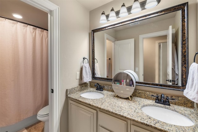 bathroom with visible vents, double vanity, a sink, and toilet