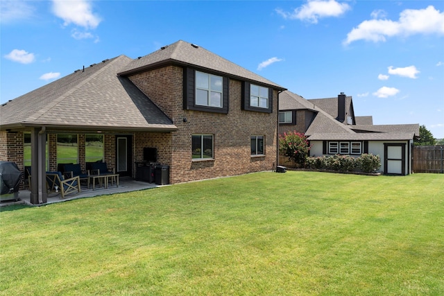 back of property featuring a shingled roof, a patio area, brick siding, and a yard