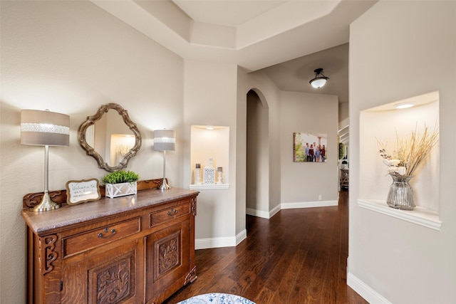 hallway featuring arched walkways, dark wood-style flooring, and baseboards