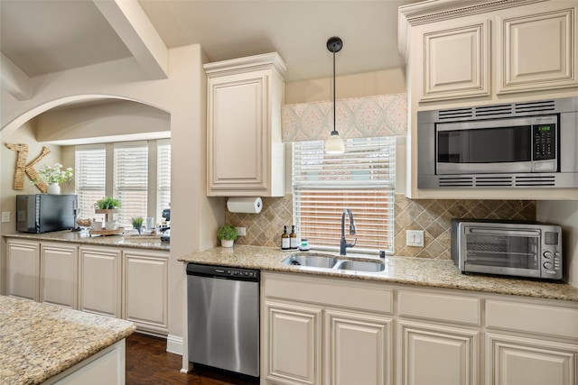 kitchen with pendant lighting, backsplash, appliances with stainless steel finishes, a sink, and light stone countertops