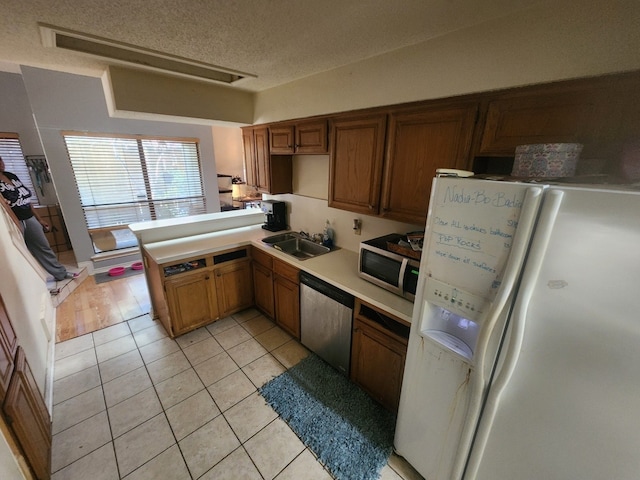 kitchen with stainless steel appliances, brown cabinetry, light countertops, and a sink