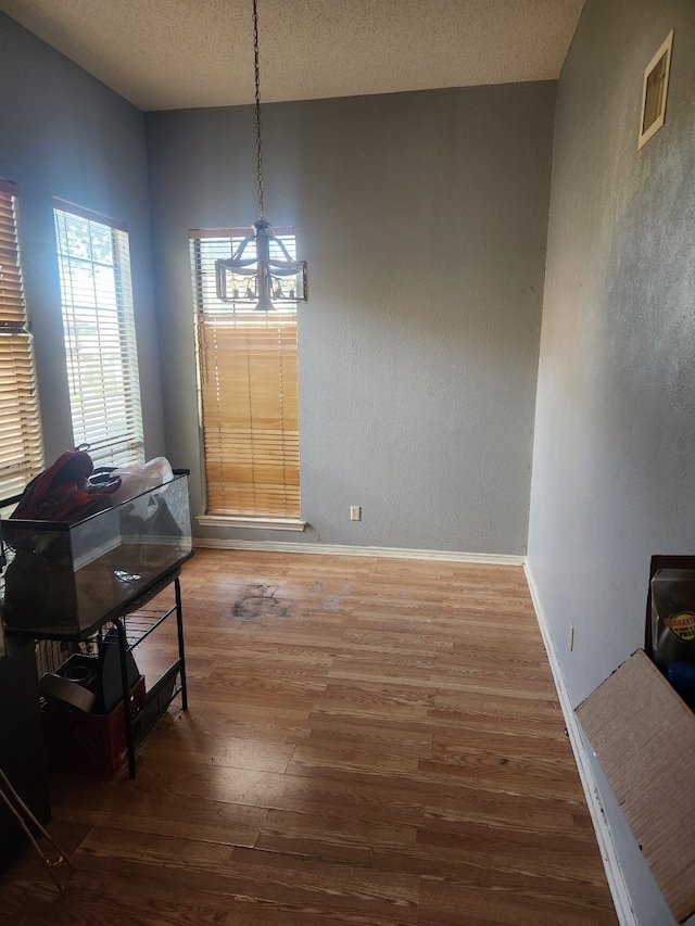 dining room with baseboards, visible vents, wood finished floors, a textured ceiling, and a notable chandelier