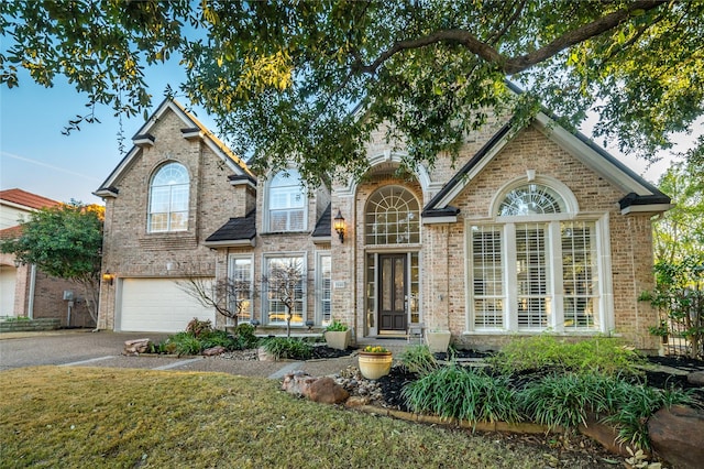 traditional-style house with an attached garage, aphalt driveway, and brick siding