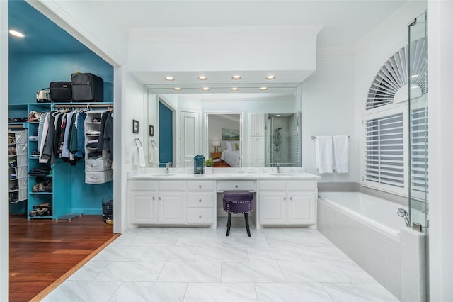 full bathroom with double vanity, a sink, a spacious closet, and a bath