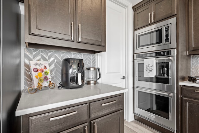1305 Redbrick Ln, Northlake, TX 76247 - kitchen featuring stainless steel appliances, dark brown cabinets, decorative backsplash, and light stone countertops
