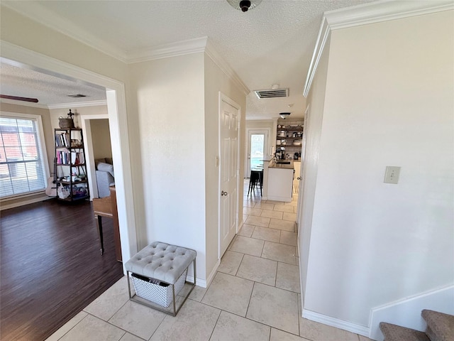 hallway with a textured ceiling, ornamental molding, visible vents, and a healthy amount of sunlight