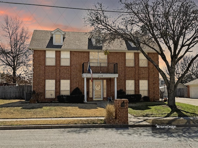 view of front facade featuring central AC unit, a balcony, brick siding, fence, and roof with shingles