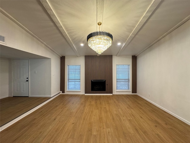 unfurnished living room featuring vaulted ceiling with beams, a large fireplace, wood finished floors, a chandelier, and baseboards