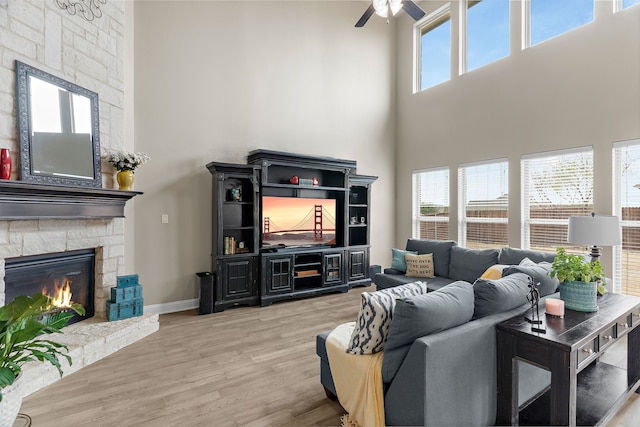 living room featuring baseboards, a stone fireplace, a wealth of natural light, and light wood-style floors