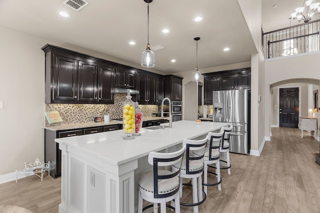 kitchen with stainless steel fridge, arched walkways, light countertops, light wood-style floors, and a sink