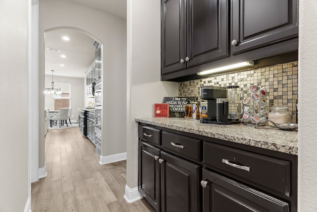 bar featuring arched walkways, visible vents, backsplash, light wood-type flooring, and baseboards