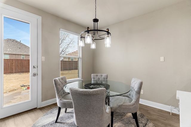 dining space with baseboards, wood finished floors, and a notable chandelier