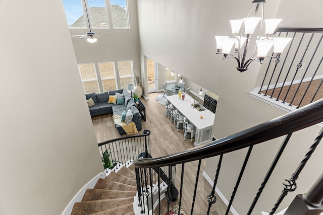 stairway with ceiling fan with notable chandelier, baseboards, a high ceiling, and wood finished floors