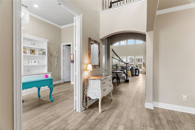 interior space with arched walkways, crown molding, a towering ceiling, light wood-style flooring, and baseboards