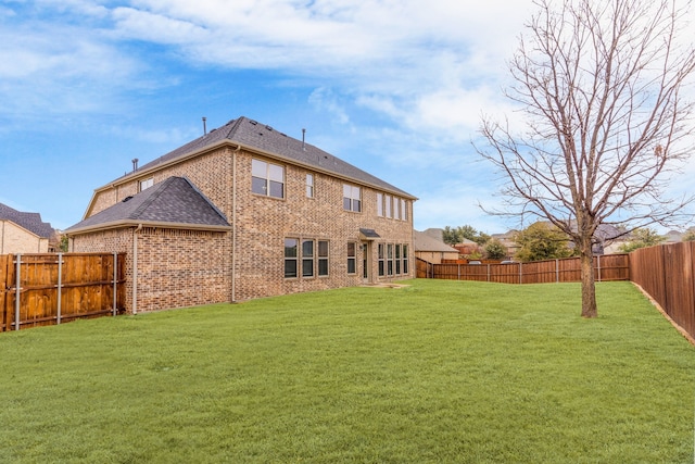 back of house featuring brick siding, a lawn, a shingled roof, and a fenced backyard