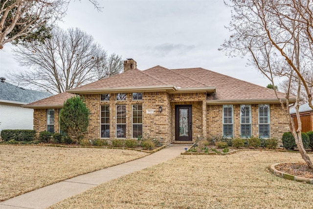 view of front of home featuring a shingled roof, a front yard, a chimney, and brick siding