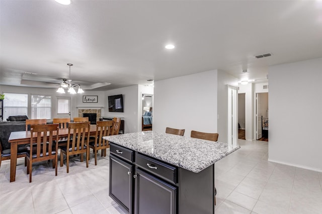 kitchen featuring ceiling fan, a kitchen island, open floor plan, a kitchen breakfast bar, and light stone countertops