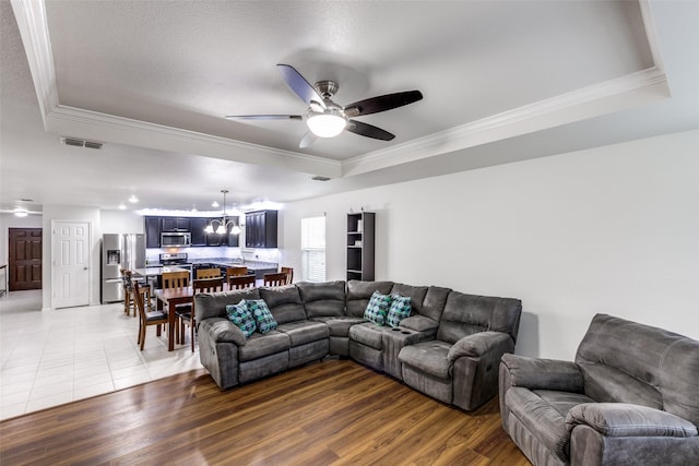 living room with ornamental molding, a tray ceiling, visible vents, and wood finished floors