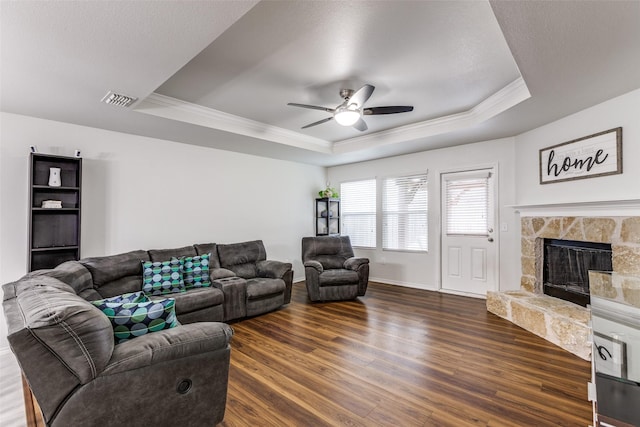 living room featuring ornamental molding, a tray ceiling, dark wood finished floors, and a stone fireplace