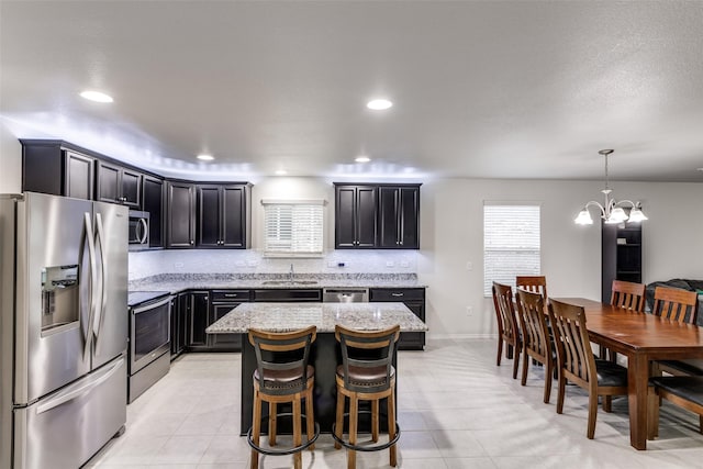 kitchen with appliances with stainless steel finishes, a center island, hanging light fixtures, and light stone countertops