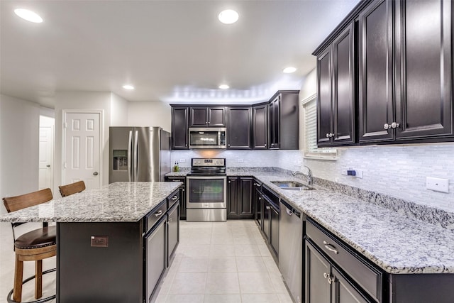 kitchen with a breakfast bar, appliances with stainless steel finishes, a kitchen island, a sink, and light stone countertops