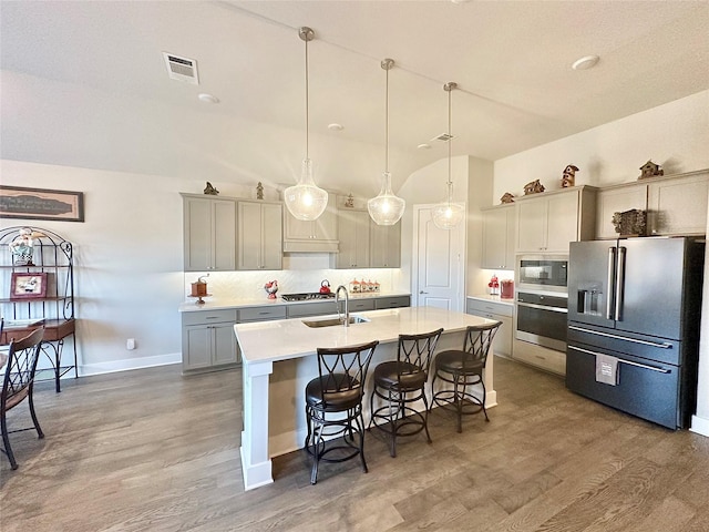 kitchen with decorative light fixtures, light countertops, appliances with stainless steel finishes, a kitchen island with sink, and a kitchen breakfast bar