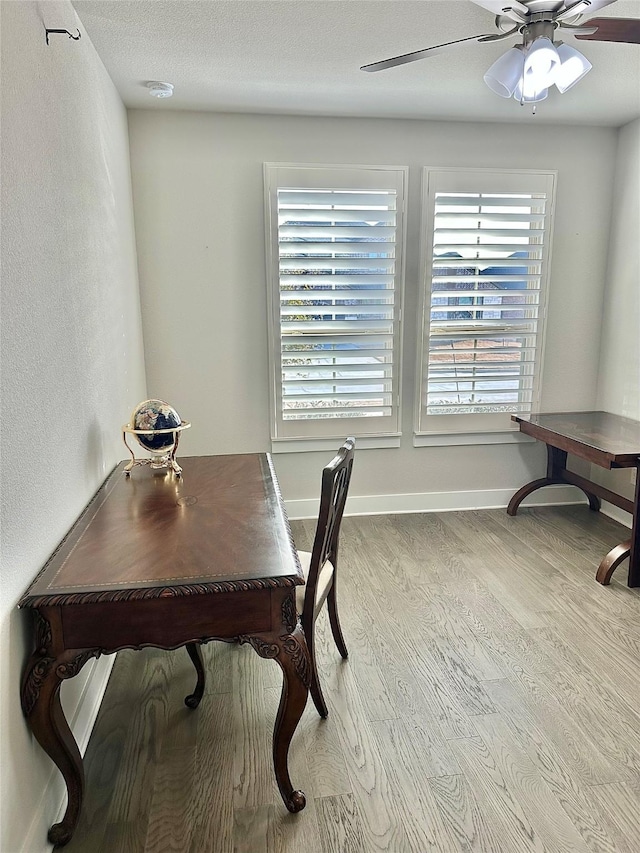 home office with light wood-style flooring, baseboards, ceiling fan, and a textured ceiling