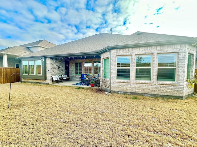 back of property featuring a shingled roof, a lawn, a patio area, and brick siding