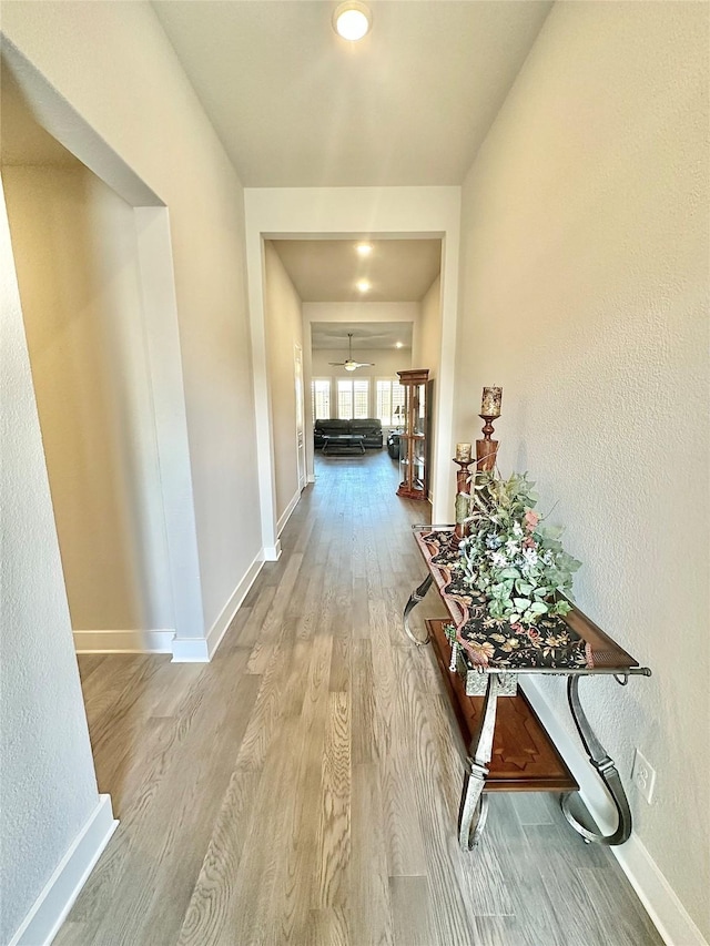 hallway featuring a textured wall, wood finished floors, and baseboards