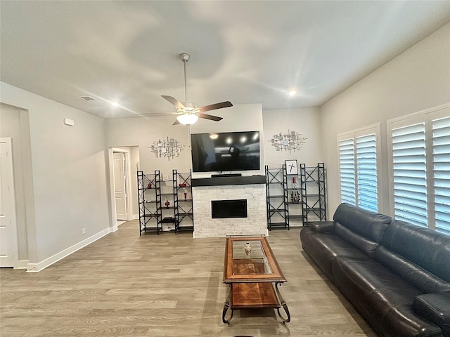 living area featuring light wood-type flooring, baseboards, a ceiling fan, and a stone fireplace