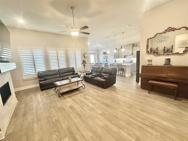 living area with light wood-style floors, ceiling fan, a fireplace, and baseboards