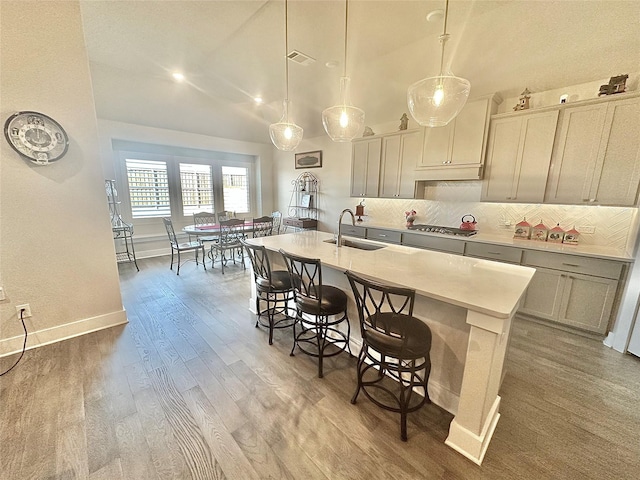 kitchen featuring tasteful backsplash, light countertops, hanging light fixtures, a sink, and an island with sink