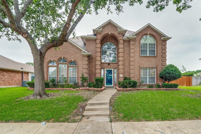 traditional home with a front yard, fence, and brick siding