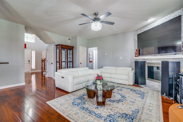 living area featuring dark wood-type flooring, a glass covered fireplace, a ceiling fan, a textured ceiling, and baseboards